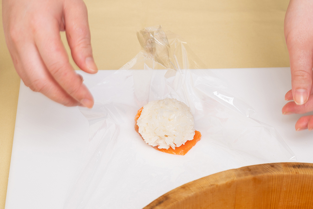 ラップにお好みの具材を載せ、その上に③の酢飯を置く。ラップで全体を包み込み、最後に口をひねって形を整える。ラップの上にネタを置き、その上にボール状の酢飯を置く。