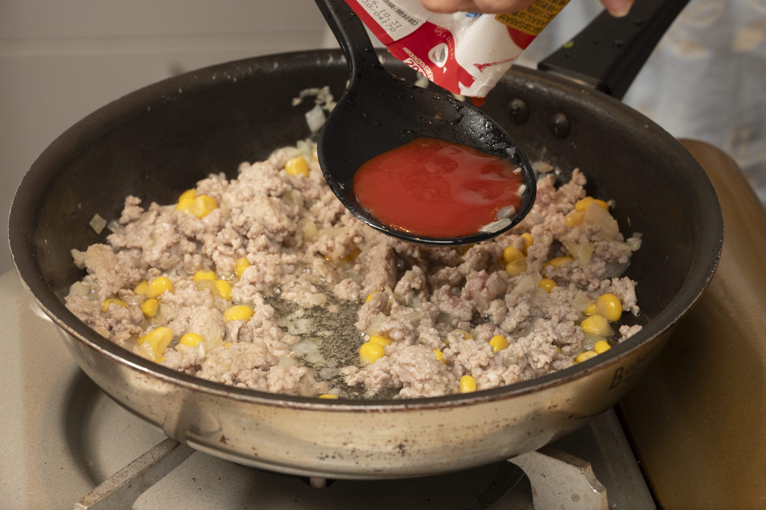 フライパンにオイルを引いて玉ねぎのみじん切り、にんにくのみじん切りを炒め、豚ひき肉をばらしながら入れて炒め、トマトジュースを加え調味料も入れる。コーンと枝豆を入れて、水分が無くなるまで加熱する